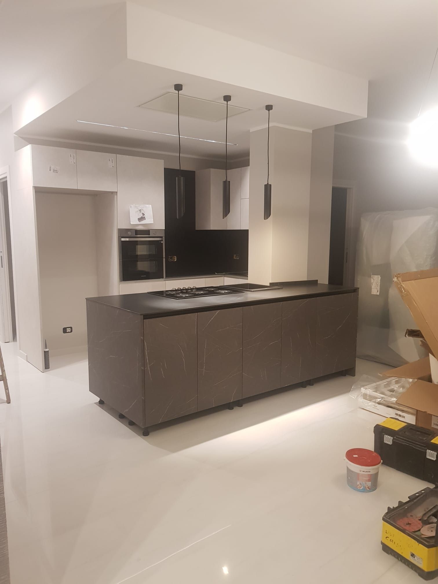 Cucina moderna con mobili scuri, isola centrale, lampade a sospensione e pavimento bianco lucido durante la ristrutturazione.