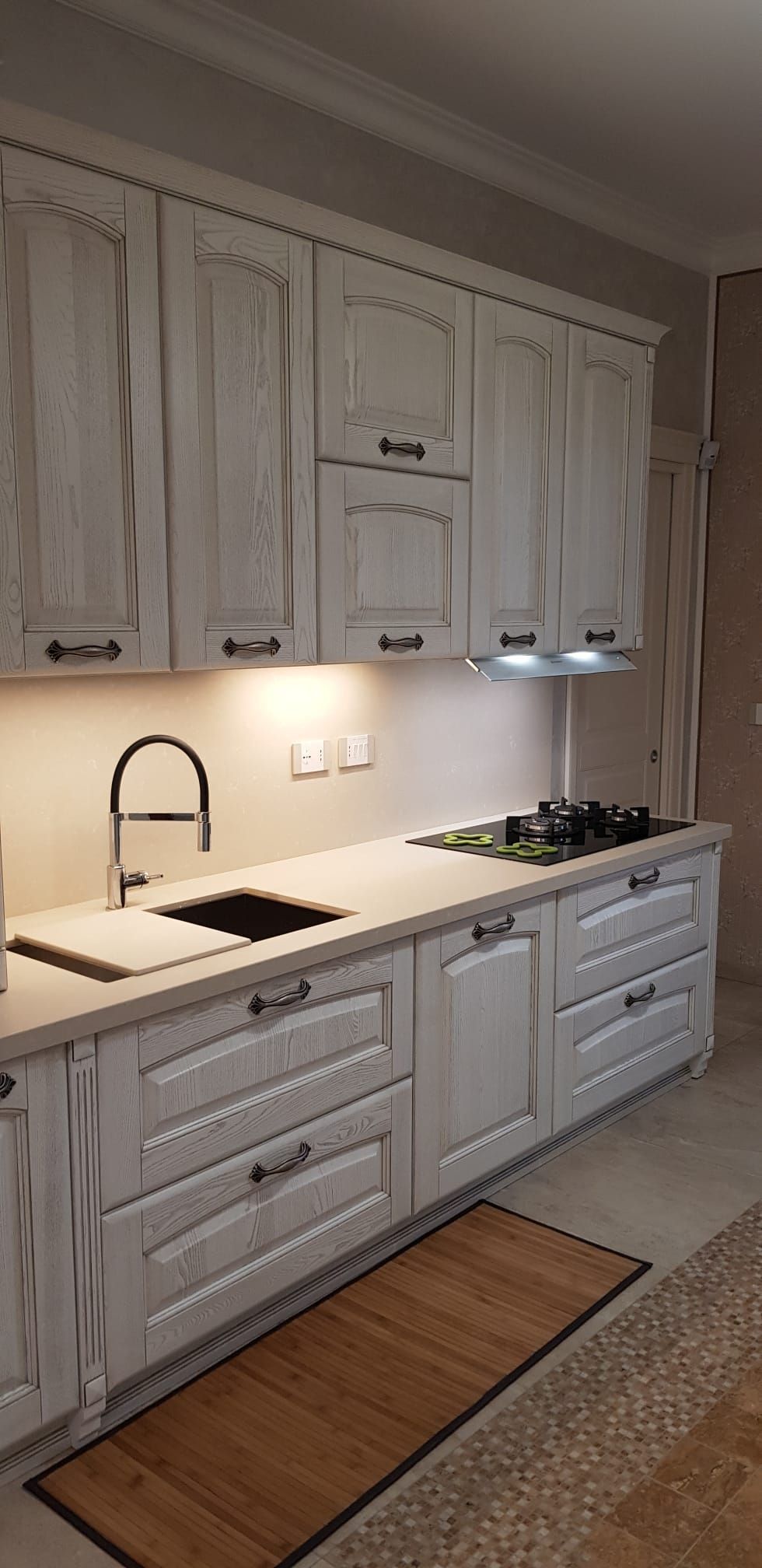 Cucina rustica bianca con mobili, piano di lavoro nero, lavello, fornelli e illuminazione sottopensile.