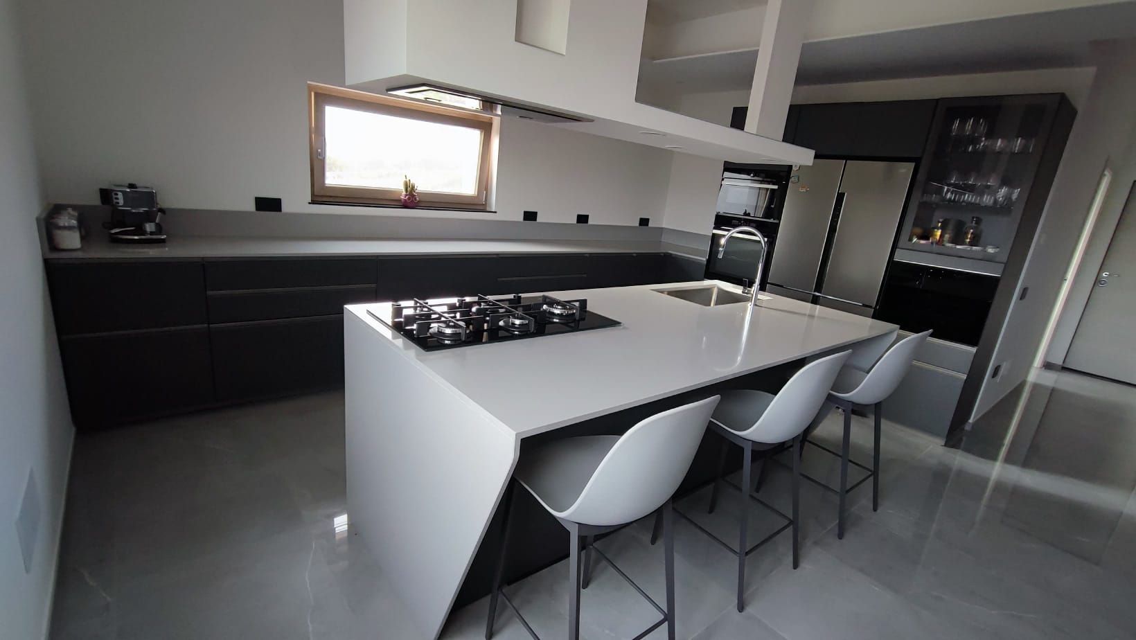 Cucina moderna con isola bianca, mobili neri, sgabelli da bar e frigorifero in acciaio inox.