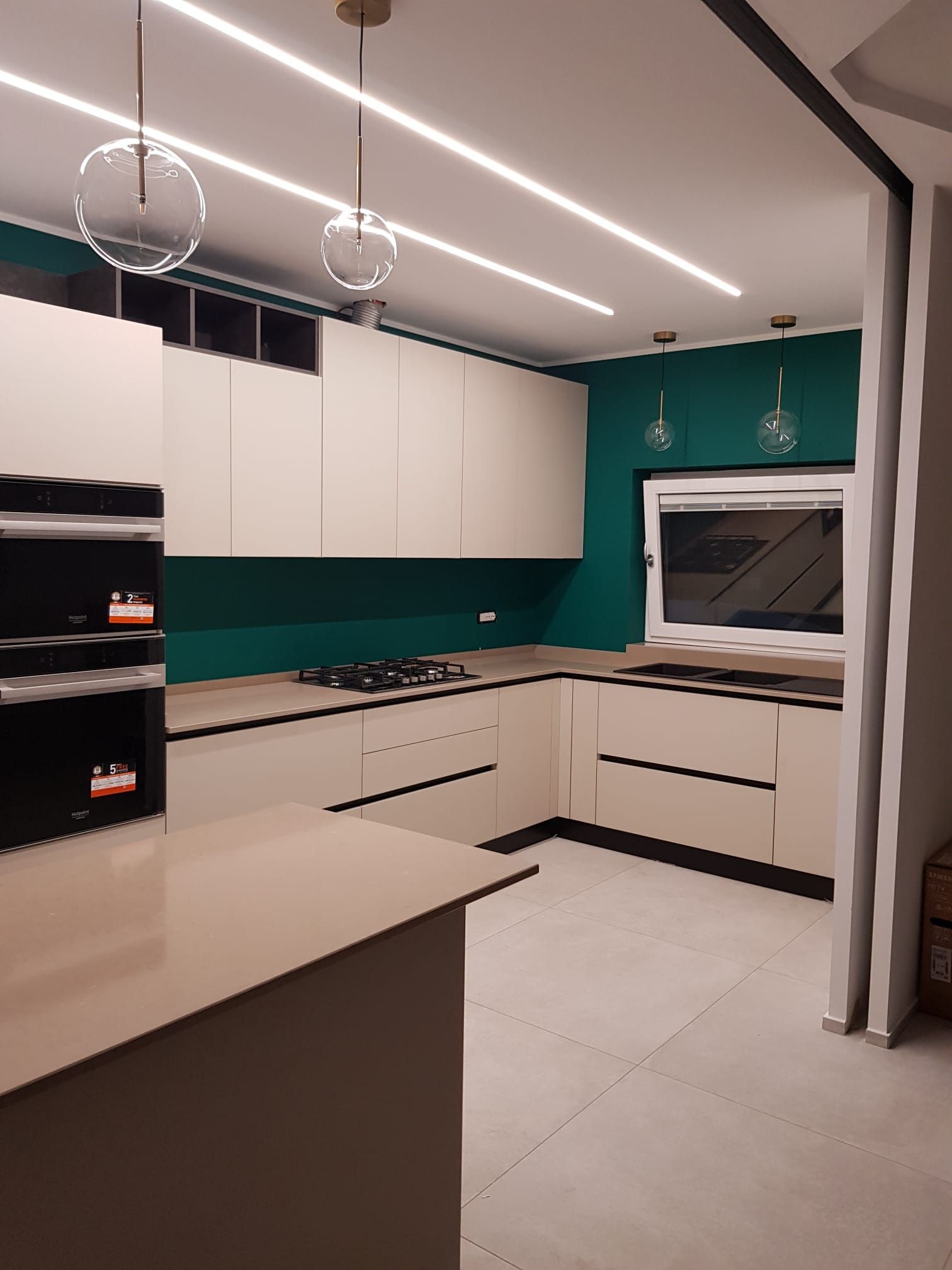 Cucina moderna con mobili color crema, paraschizzi color verde acqua, forno a incasso e lampade a sospensione.