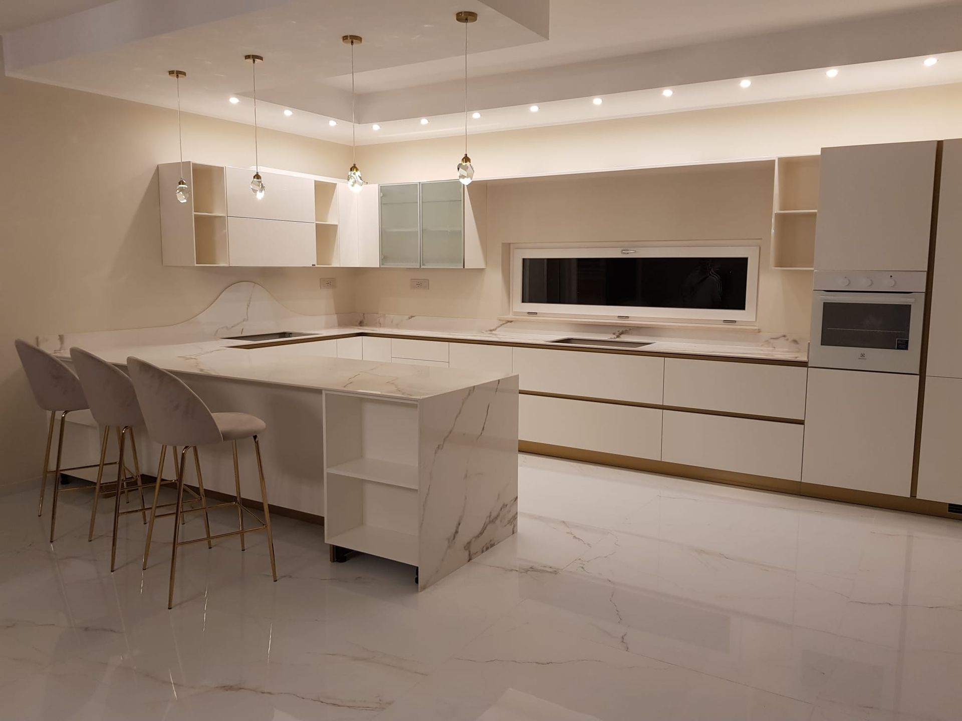 Cucina moderna bianca con isola, sgabelli da bar ed elettrodomestici a incasso, illuminata da una luce calda.