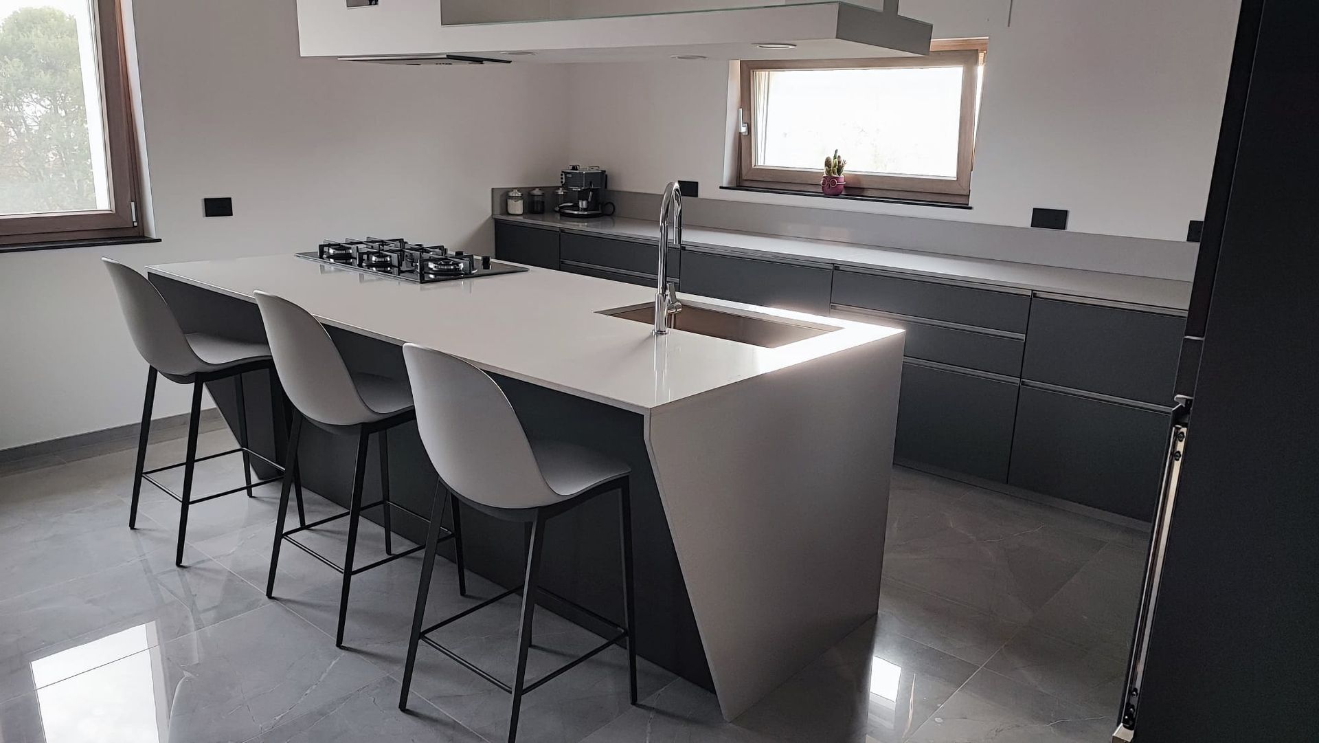 Cucina moderna con un'ampia isola, sgabelli e mobili scuri vicino a una finestra.