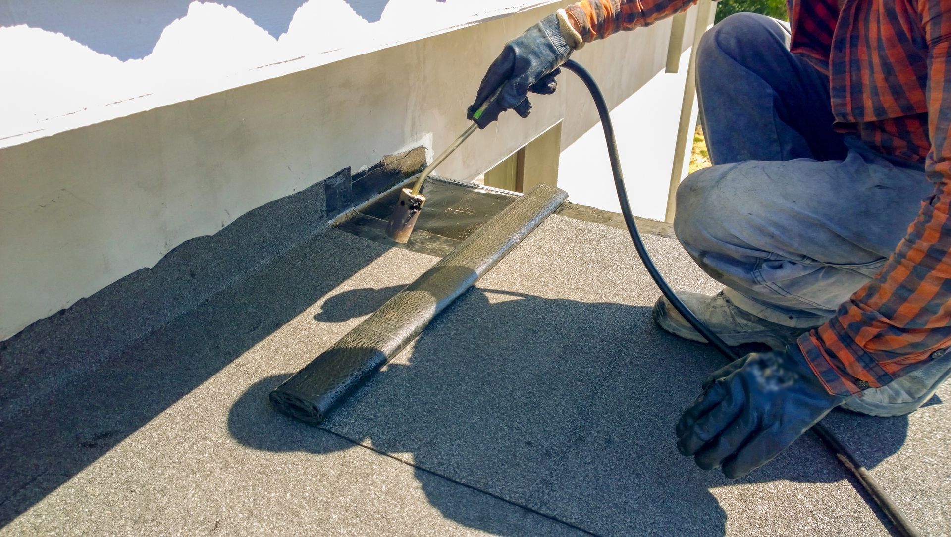 Person in gloves using a torch to seal roofing material.