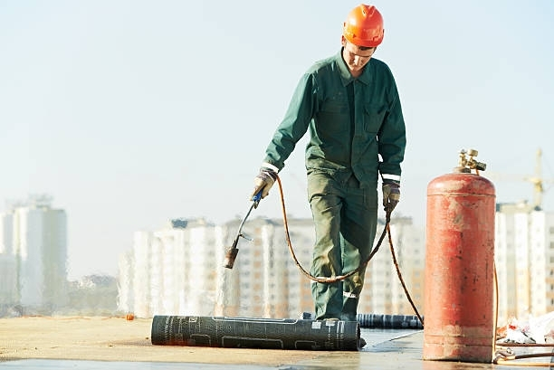 Roofer using a torch to install roofing material on a flat roof.