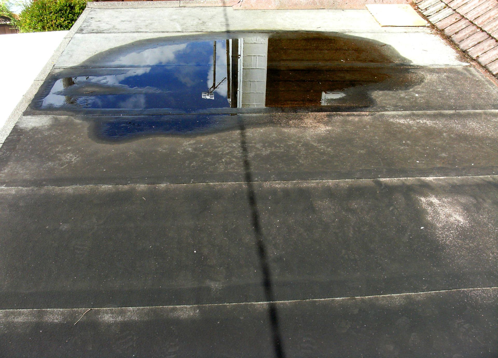 Flat, dark roof with a large puddle reflecting the sky and a building.