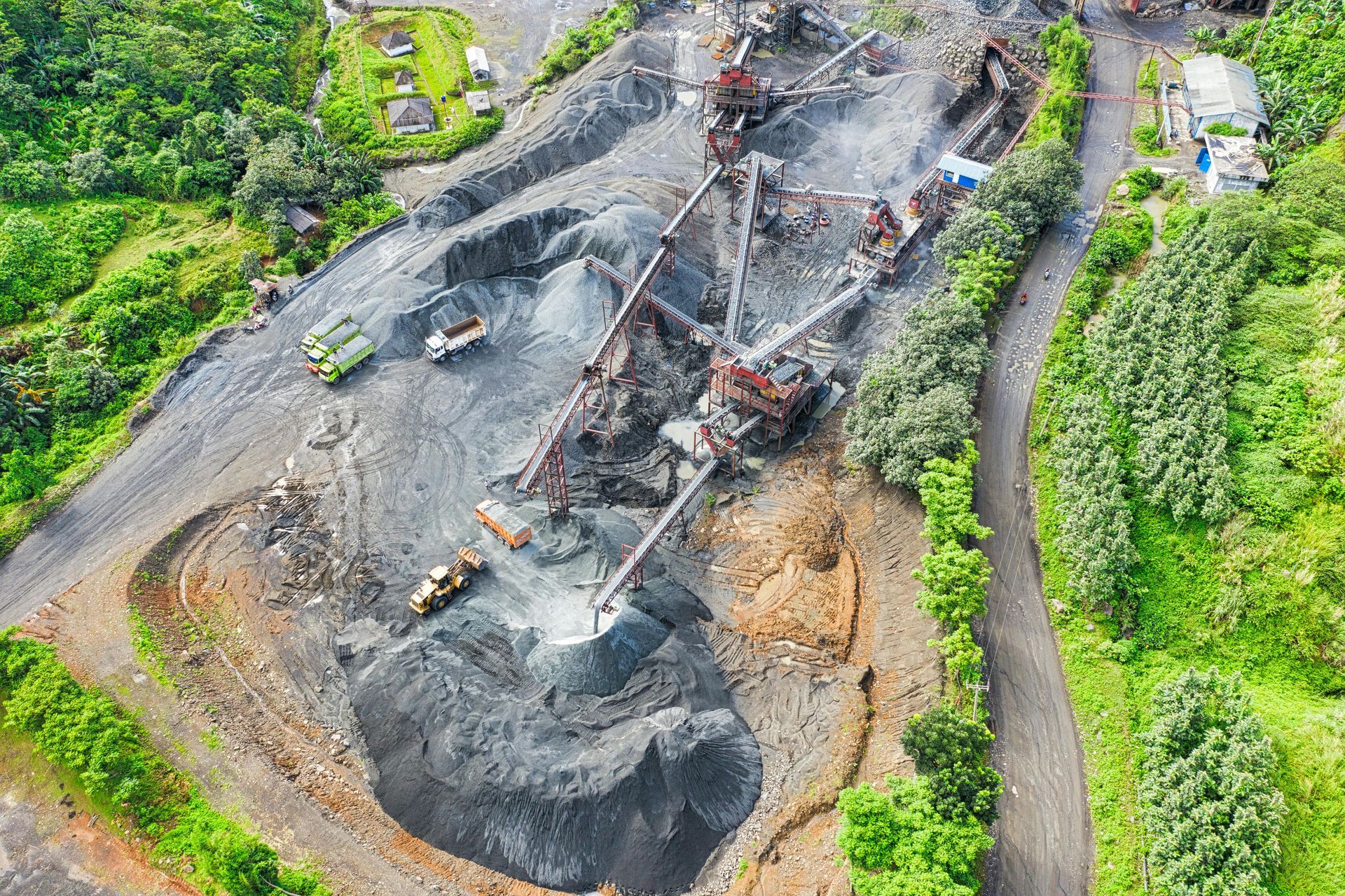 Aerial view of a quarry with machinery, trucks, and piles of gravel and rock; surrounded by green vegetation.