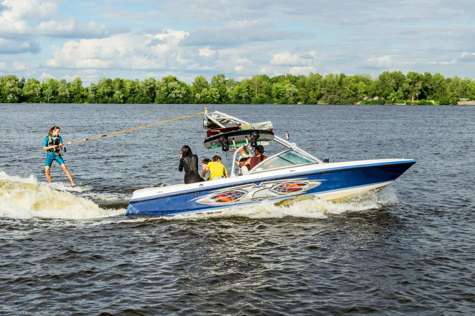 Wakeboarder being towed by a blue-and-white speedboat on a lake under a cloudy sky