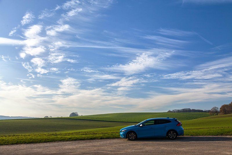 A blue car is parked on the side of a road in a field.