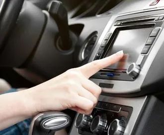 Person's hand touching a touchscreen in a car's dashboard, near steering wheel and controls.