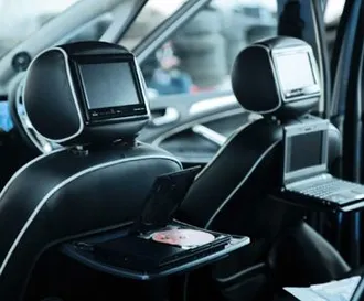 Car interior with headrest screens, DVD player, and laptop mounted on back of seats.
