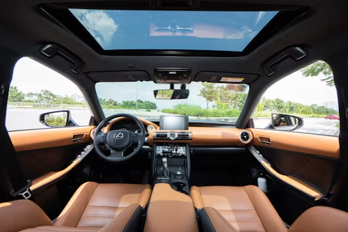 Luxury car interior with tan leather seats, panoramic sunroof, and dashboard view from the back seat