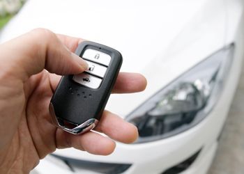 A person is holding a car key in front of a white car.