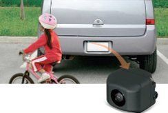 A little girl is riding a bike next to a car in a parking lot.