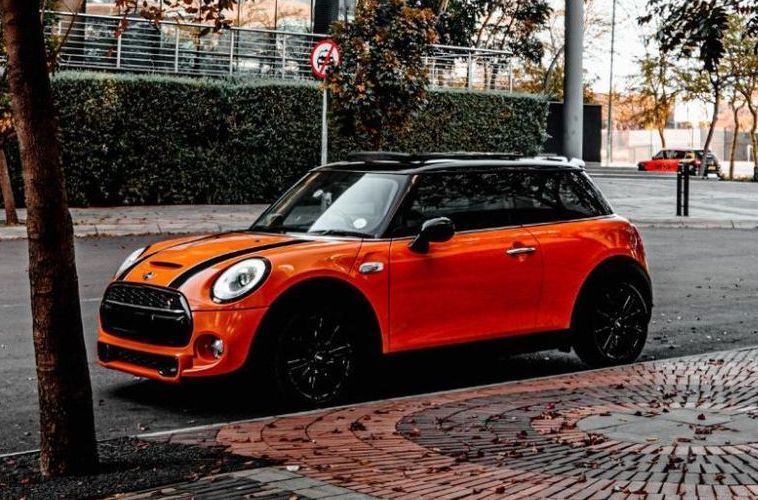 A red mini cooper is parked on the side of the road next to a tree.
