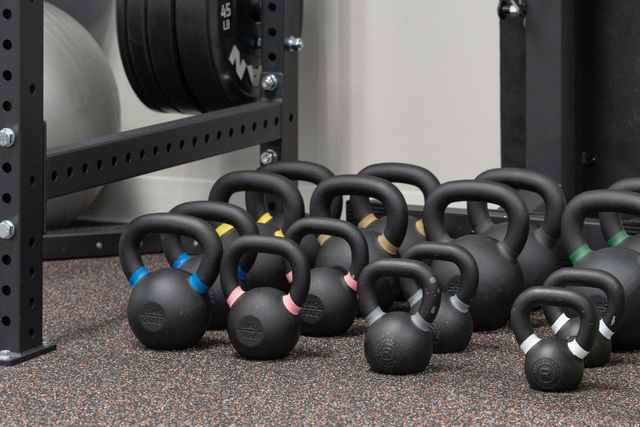 Kettlebells of various sizes lined up on a gym floor beside weight racks.