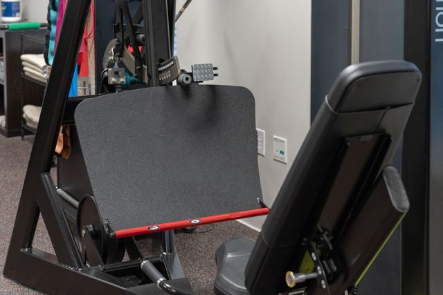 Black exercise seat and backrest on a home gym machine with red frame and monitor screen