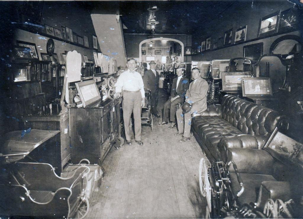 Vintage black-and-white shop interior with two men among furniture, lamps, and antique items