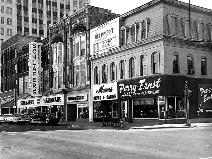 Historic city street with storefronts and signs, including Perry Bros. and a parked bus.