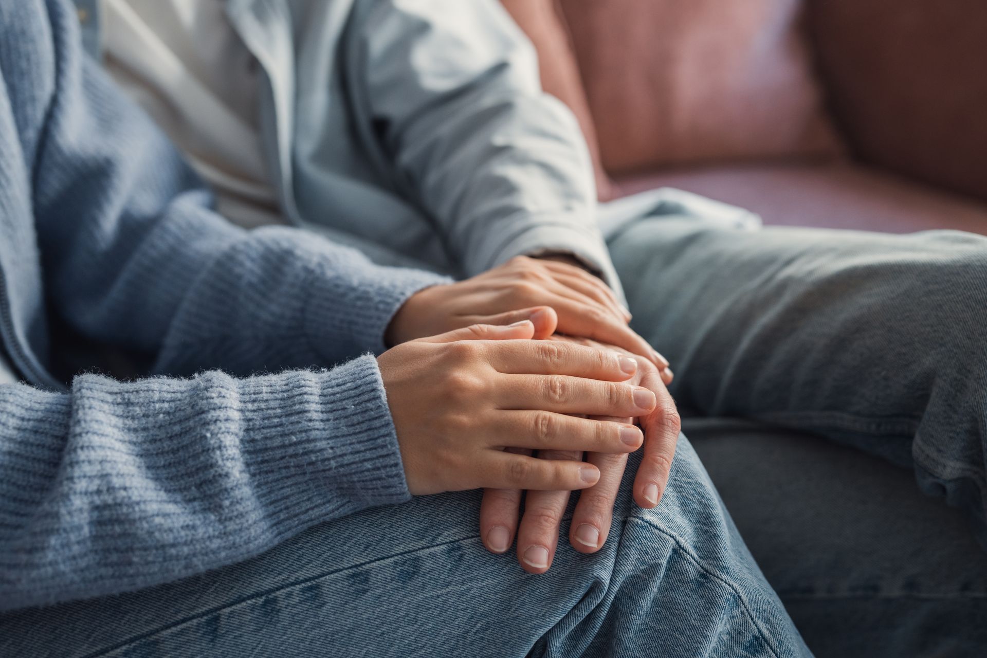 Hands clasped in a comforting gesture on a lap, with a blue sweater and jeans visible.
