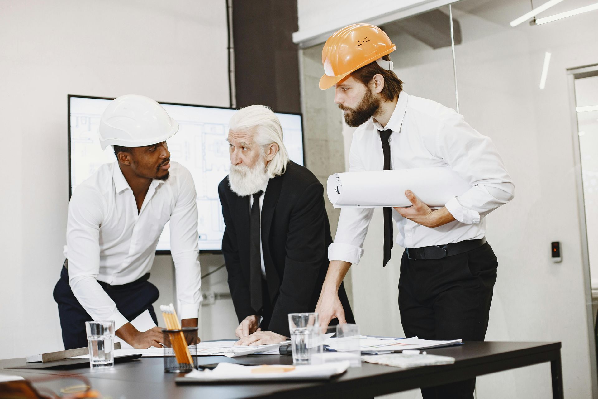 Three coworkers in hard hats reviewing plans at a construction site conference table.