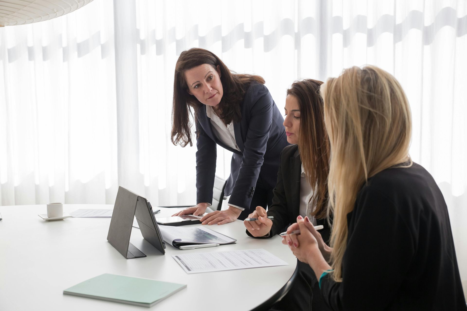 Three coworkers meeting at a white table with a tablet and documents in a bright office