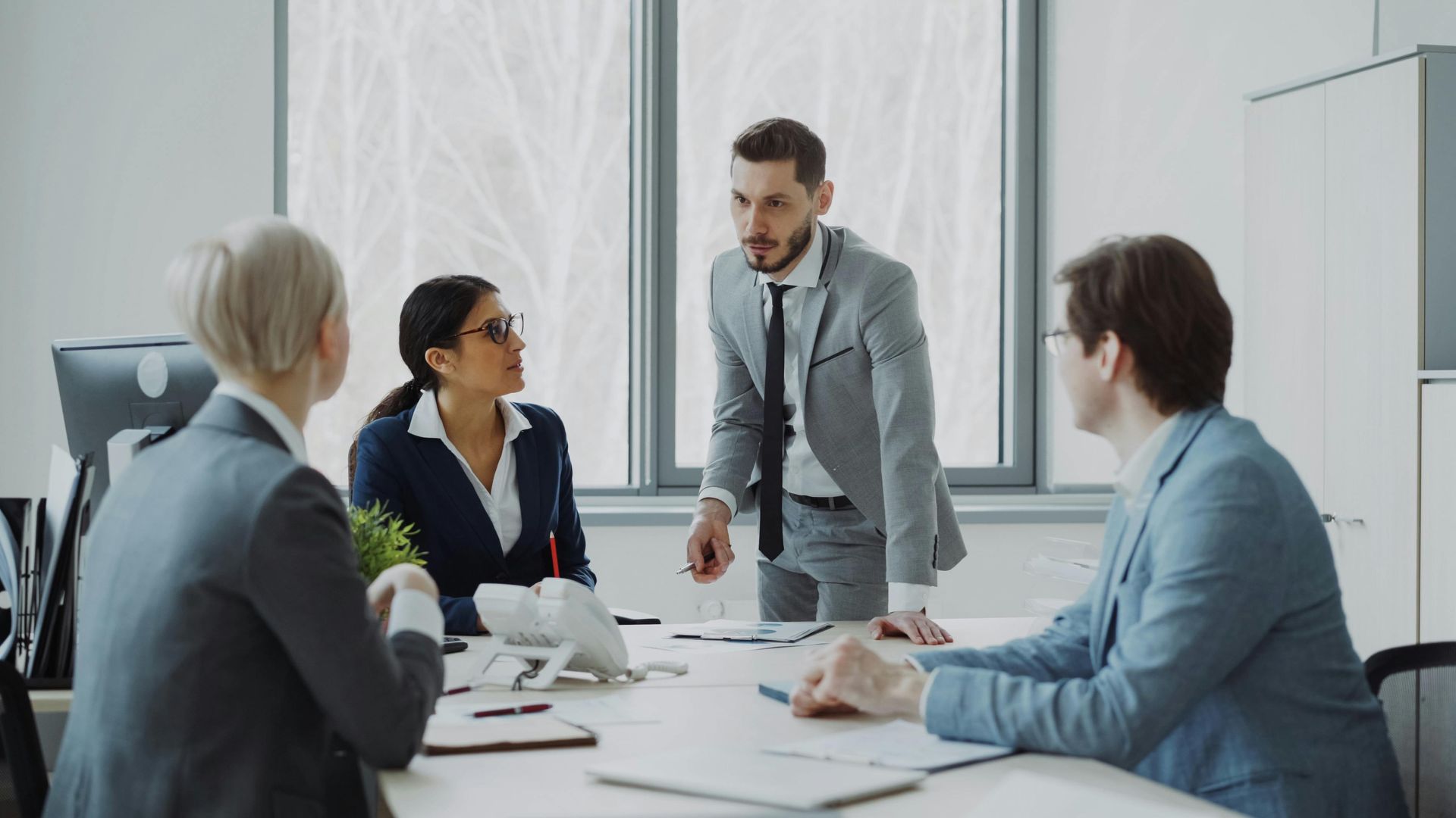 Business meeting in a bright office, with four colleagues discussing around a conference table.
