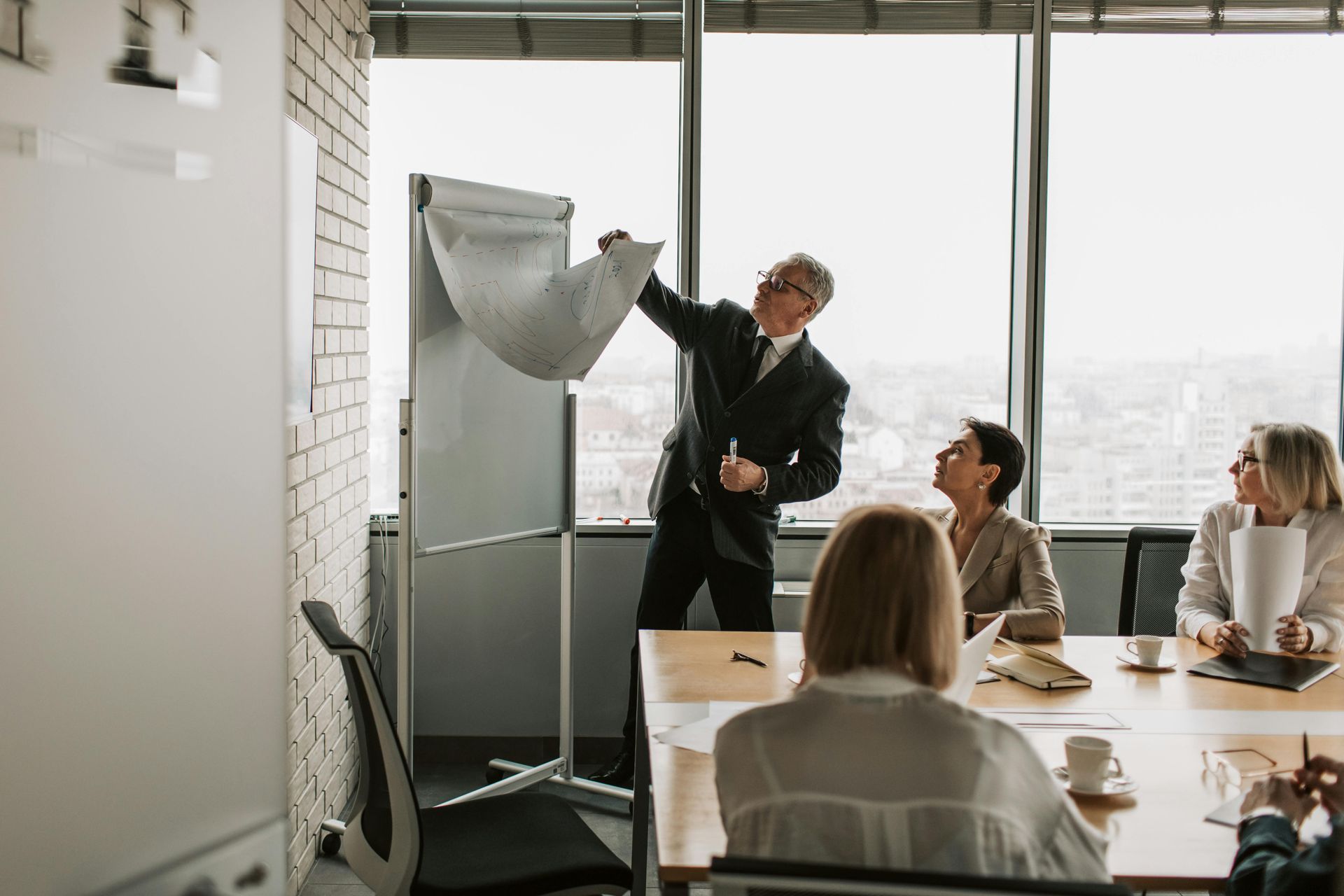 Presenter speaking beside flip chart in a bright meeting room with seated coworkers