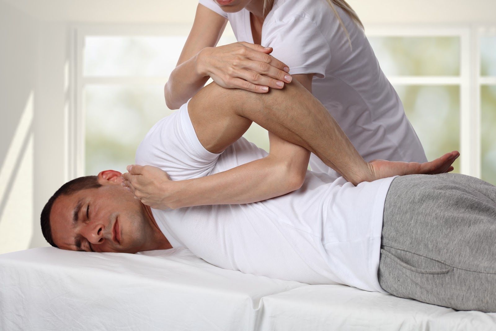 Massage therapist stretching a man lying on a table in a bright room