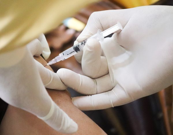 Gloved hands giving an injection with a syringe into a patient’s arm