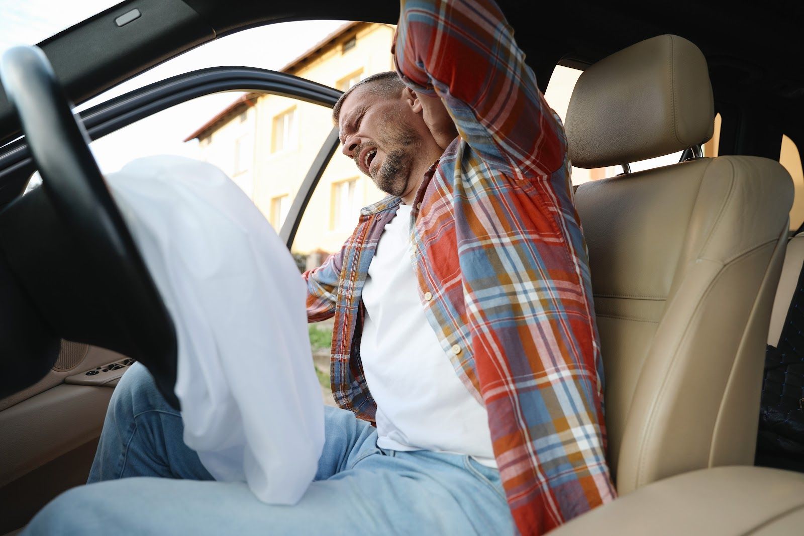 Man stretching in the driver’s seat of a car, holding a white cloth or bag