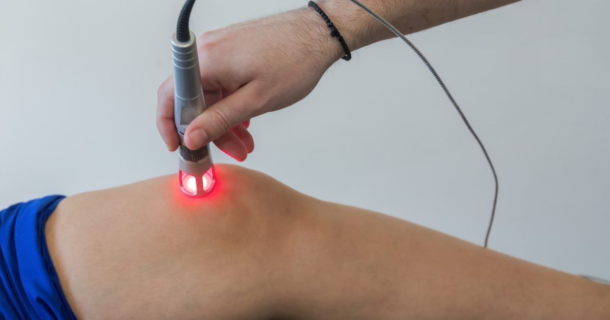 Hand-held laser treatment on a person's knee, with a red light on the skin.