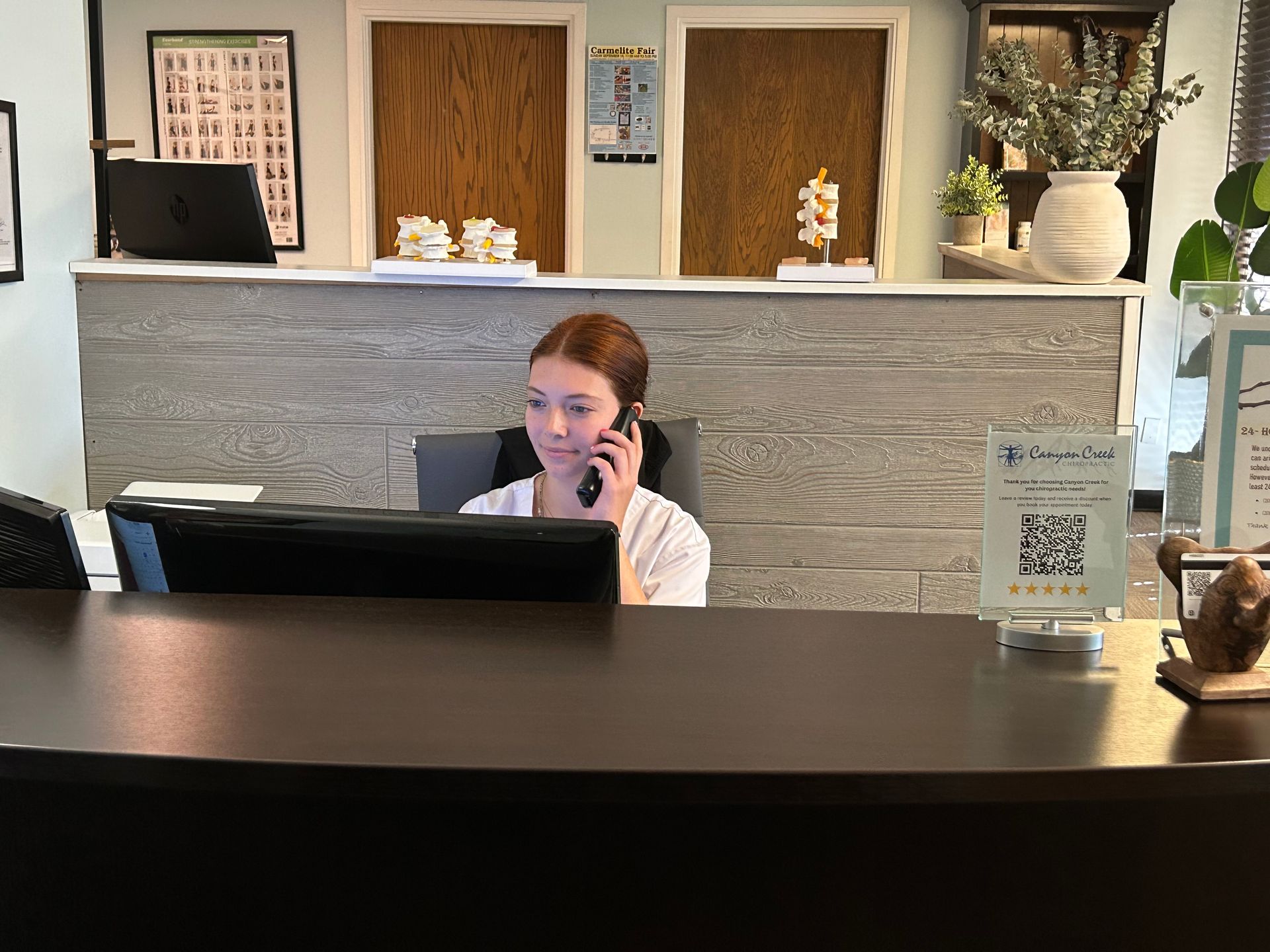 Hotel receptionist at a front desk, speaking on the phone behind a monitor and counter.