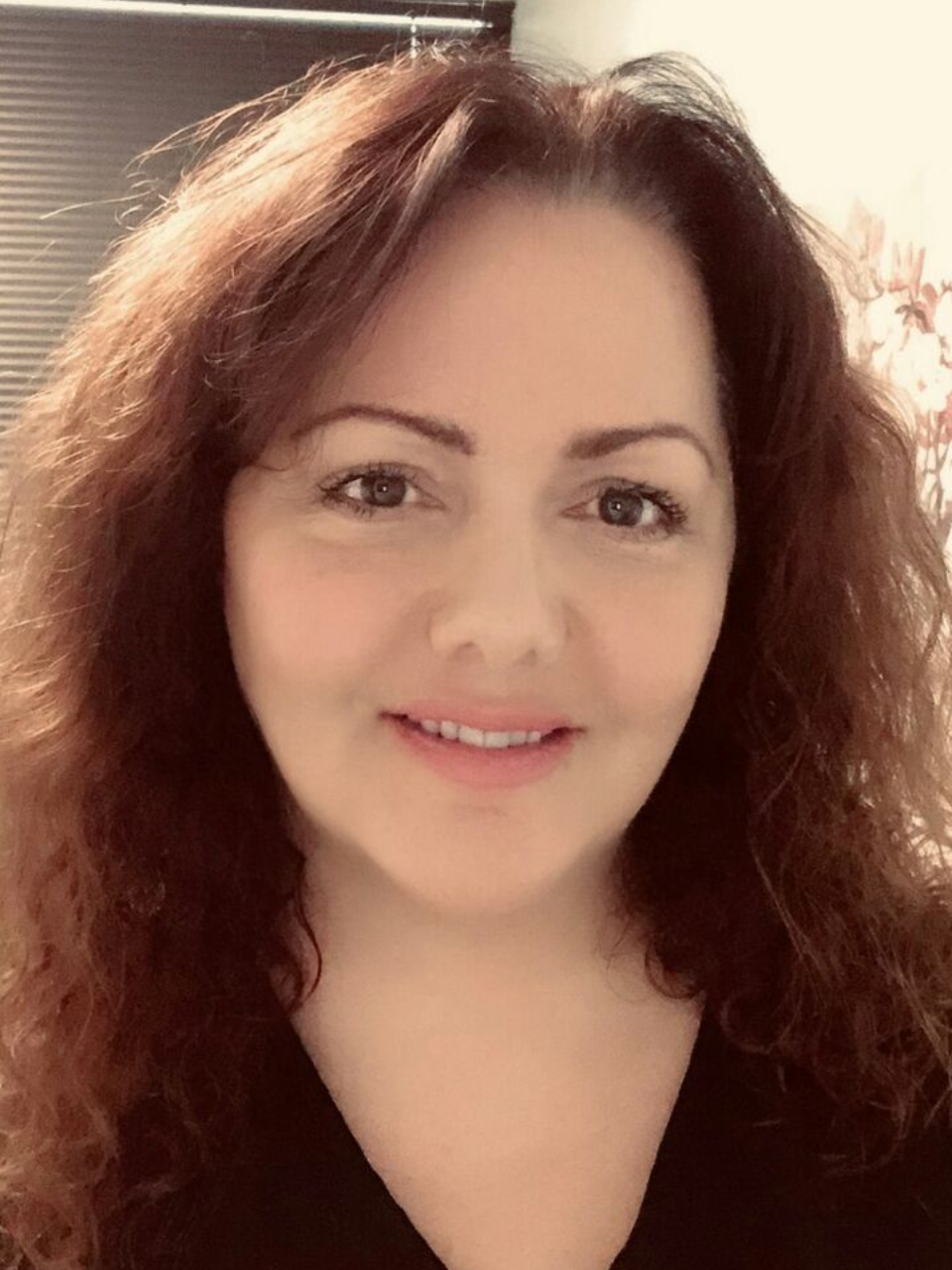 Portrait of a smiling person with curly brown hair in soft indoor light