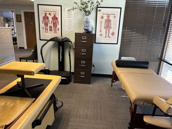 Physical therapy treatment room with two tables, exercise equipment, wall anatomy charts, and a filing cabinet.