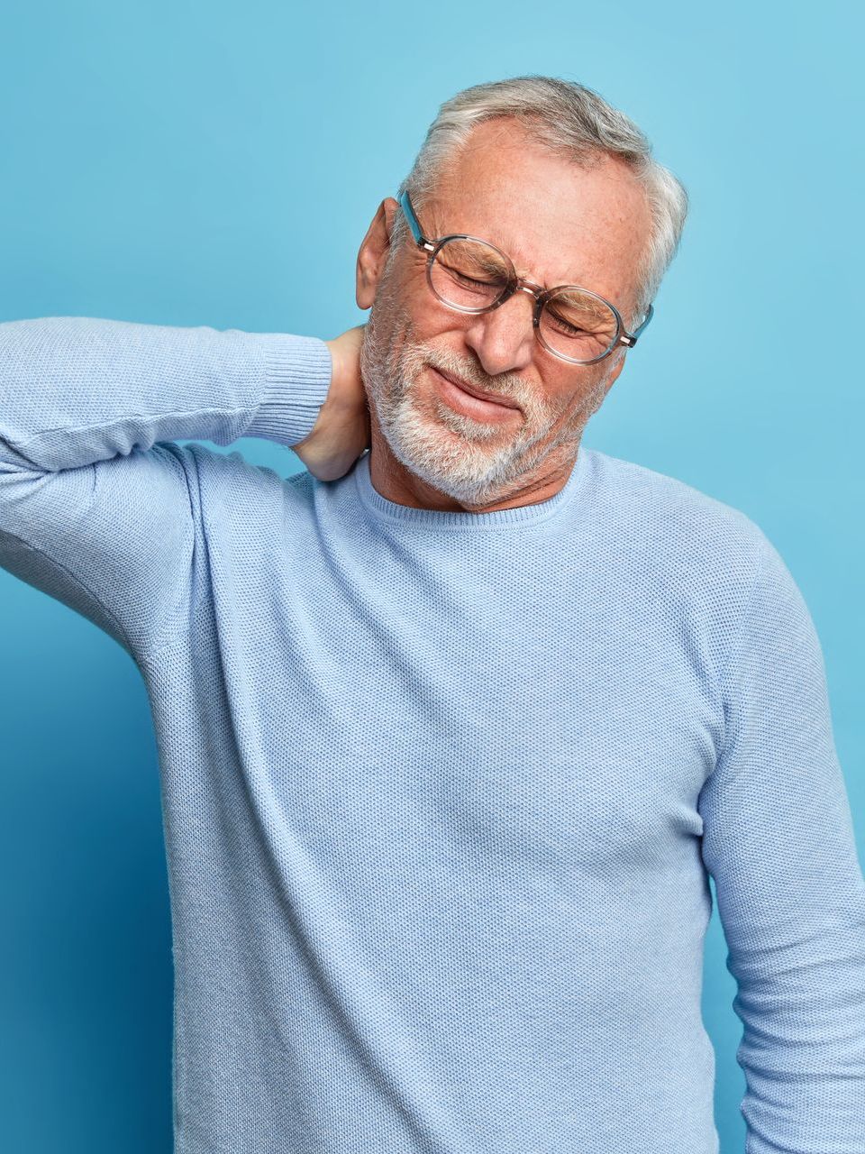 An older man with glasses is holding his neck in pain.