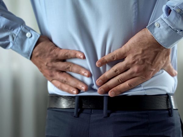 Man in blue shirt holding his lower back, suggesting back pain