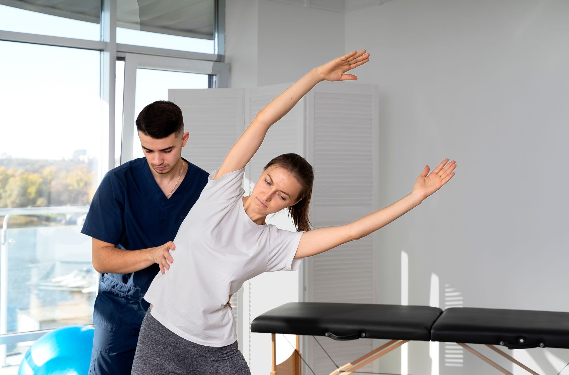 a man is helping a woman stretch her arms in a hospital .
