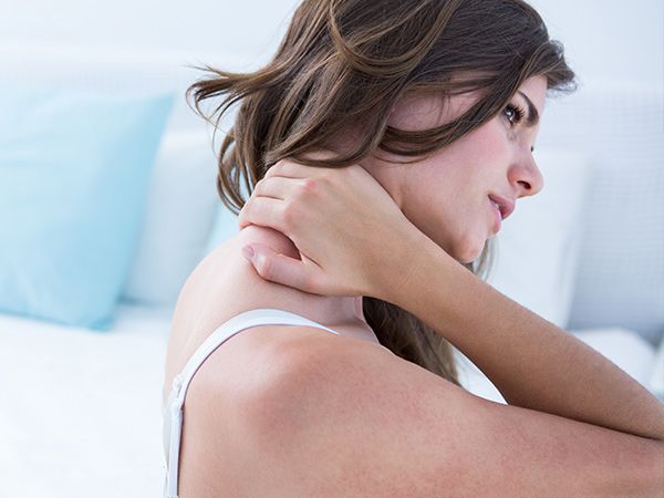 a woman is sitting on a bed holding her neck in pain .