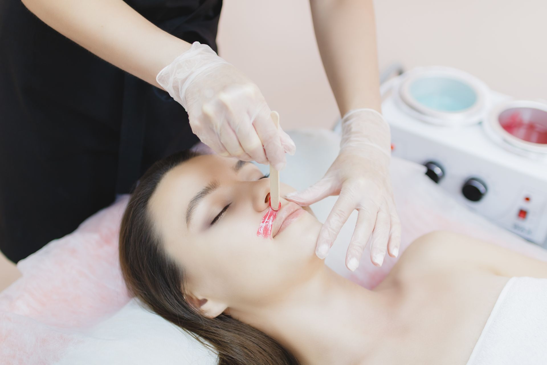 Gloved esthetician applying a treatment to a woman's face in a spa treatment room