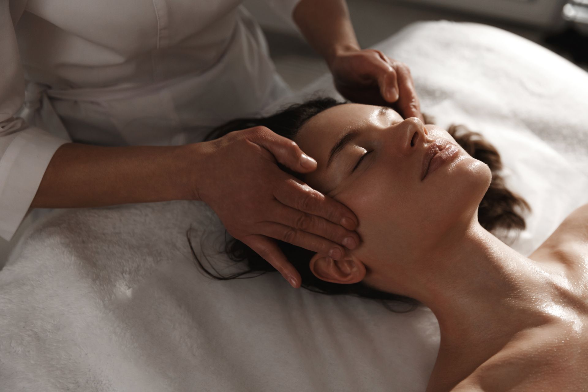 Massage therapist gently massaging a woman’s face on a treatment table