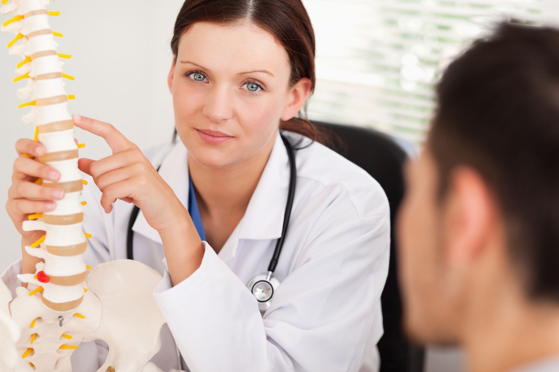 a doctor is holding a model of a spine and talking to a patient .