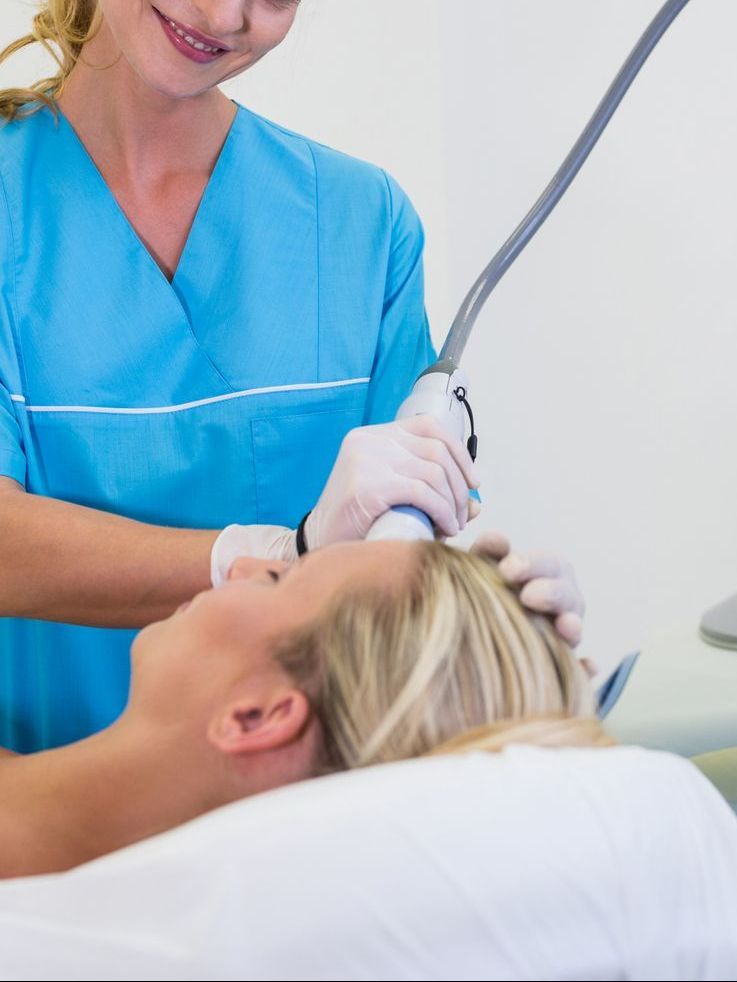 Dental hygienist in blue scrubs using a dental tool on a reclining patient