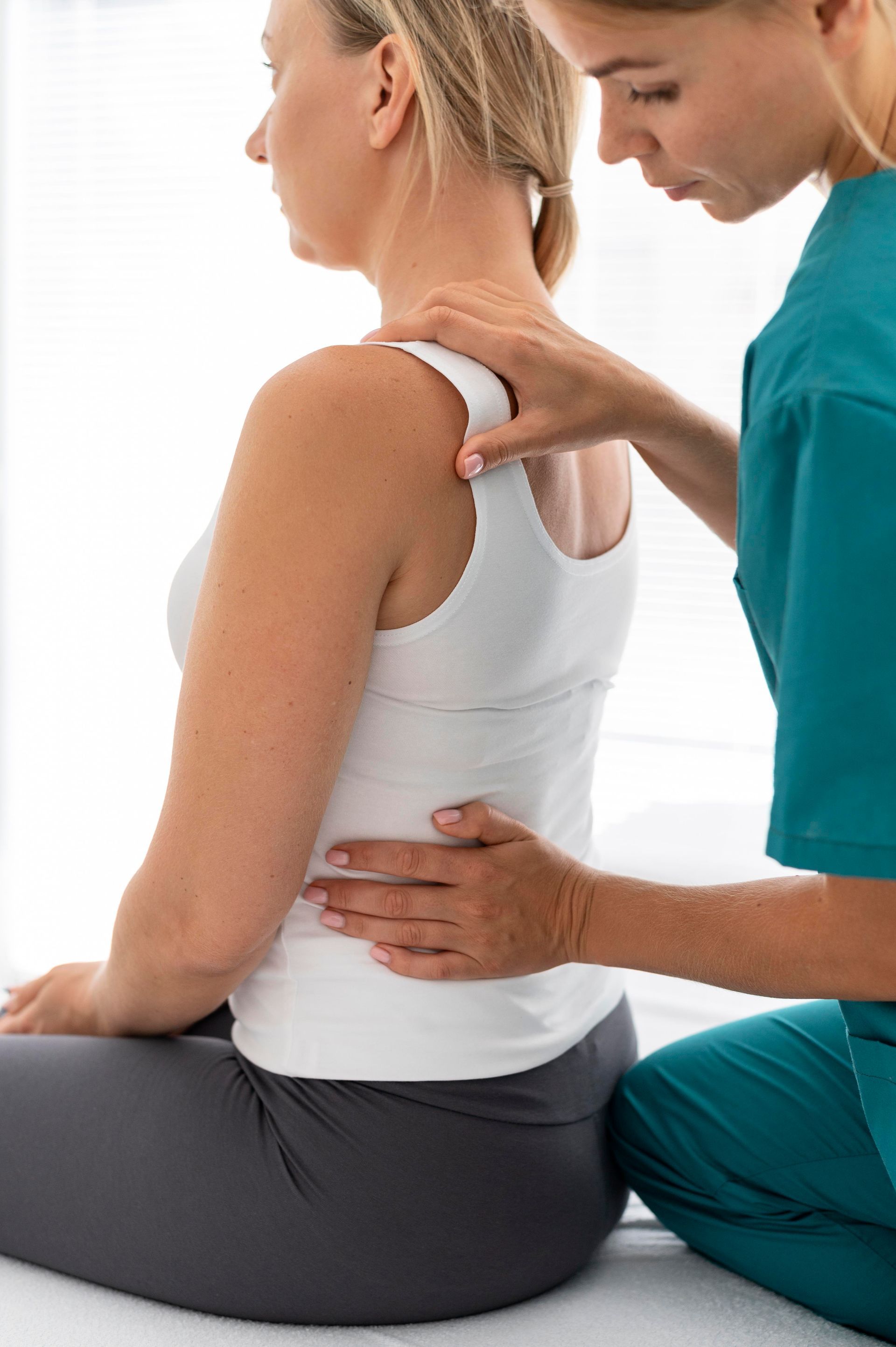 Physical therapist treating a seated patient’s shoulder and back during a therapy session