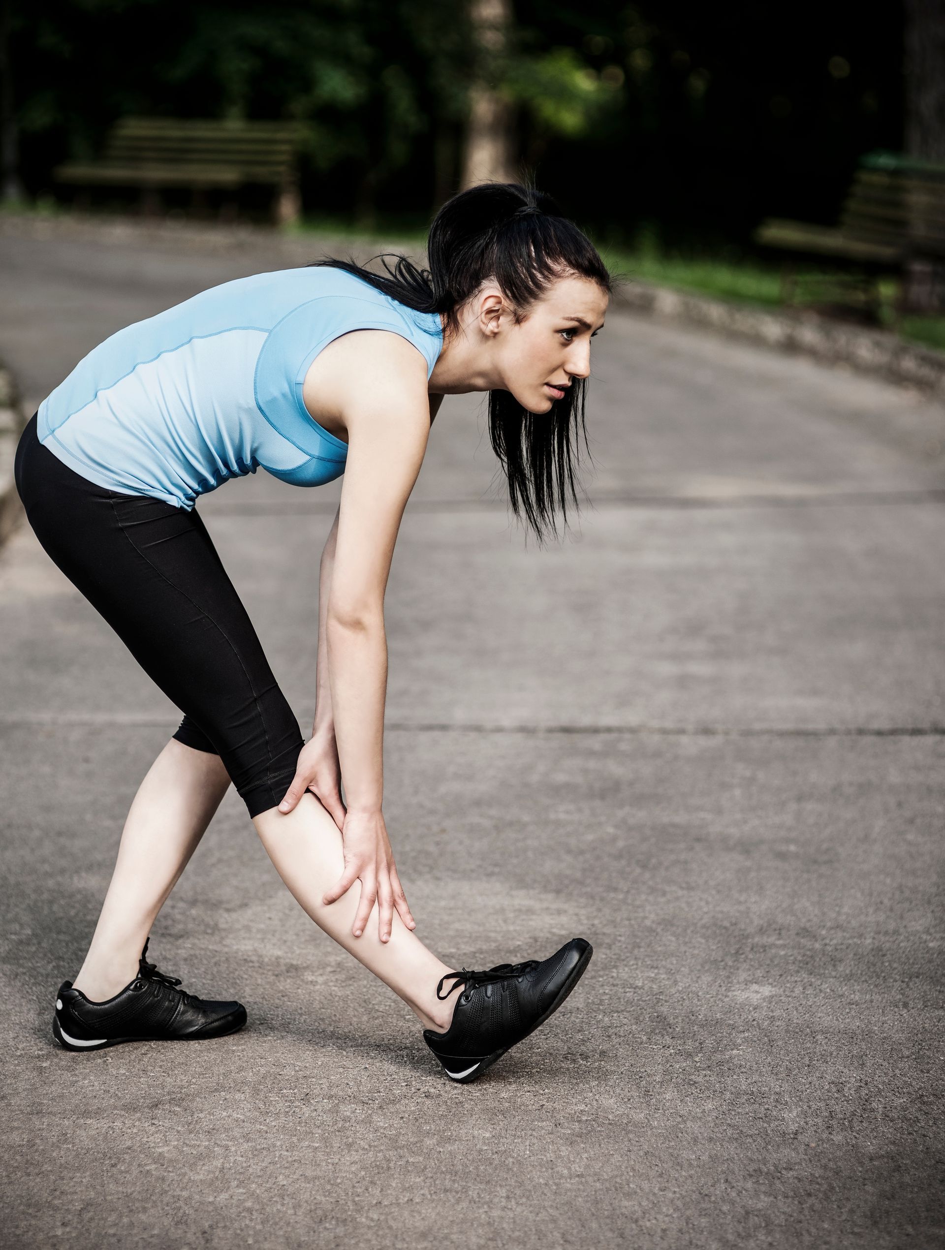 A woman in a blue tank top is stretching her leg