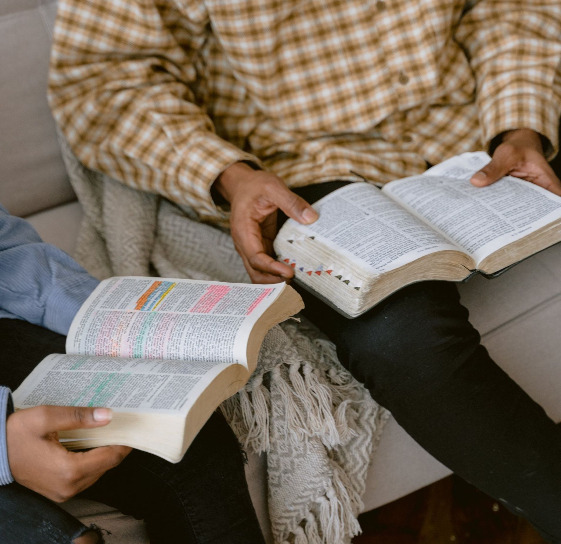 Two people are sitting on a couch reading the Bible