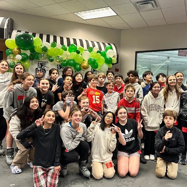 Group of smiling students posing indoors with green and gold balloon decorations behind them