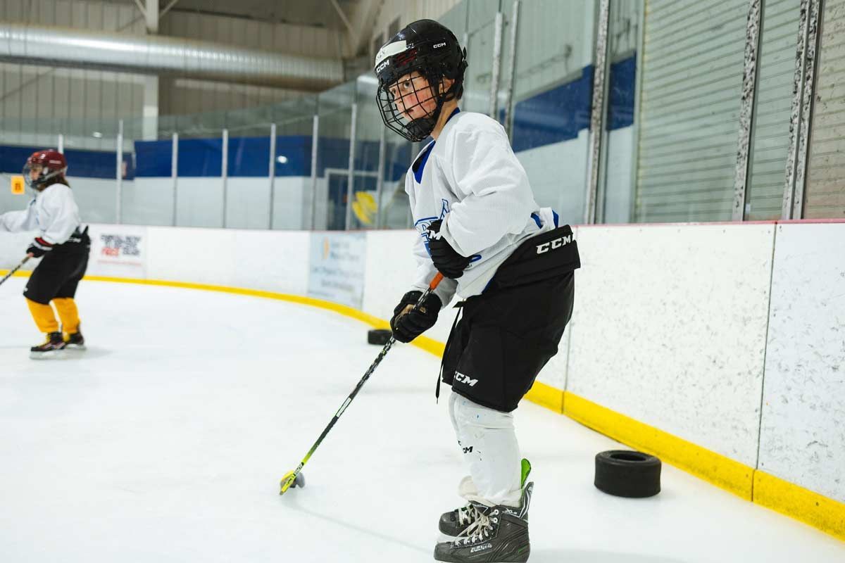 Hockey player in white jersey and black pants handling a puck on an indoor rink