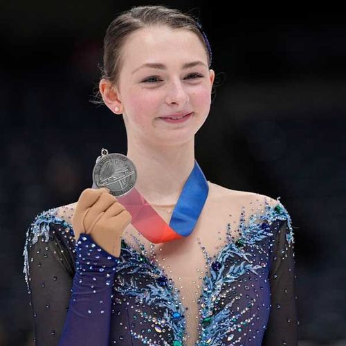 Figure skater in blue costume holding a silver medal and smiling on the ice