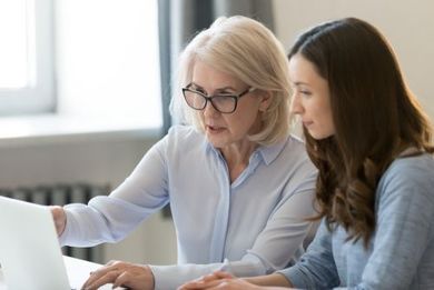 Two women reviewing a laptop together at a bright office desk