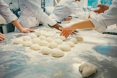 Hands kneading dough balls on a floured bakery worktable